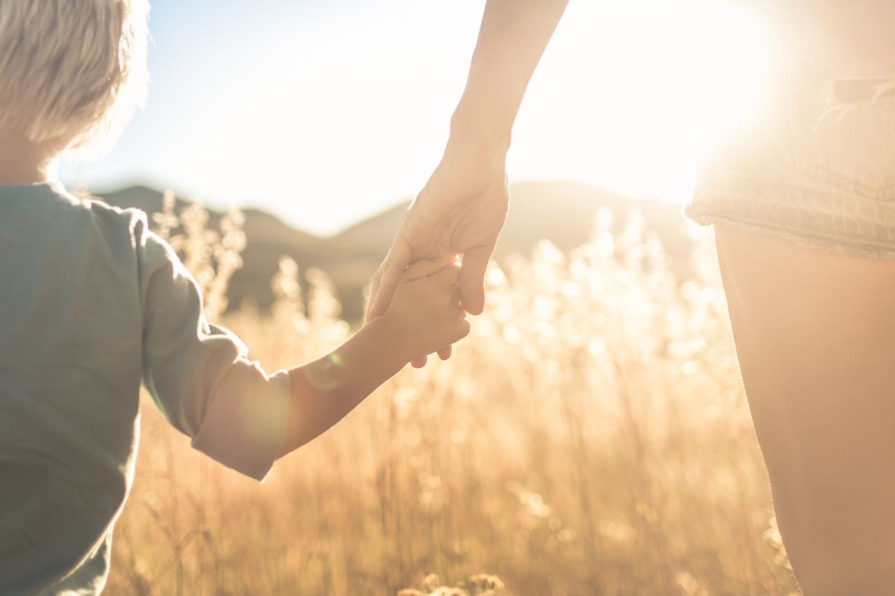 Mother and son holding hands walking at sunset.